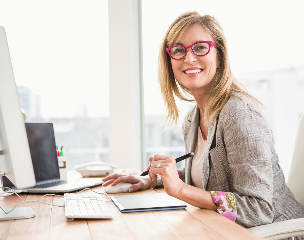 A women looking at that camera, sitting at a desk, doing paperwork
